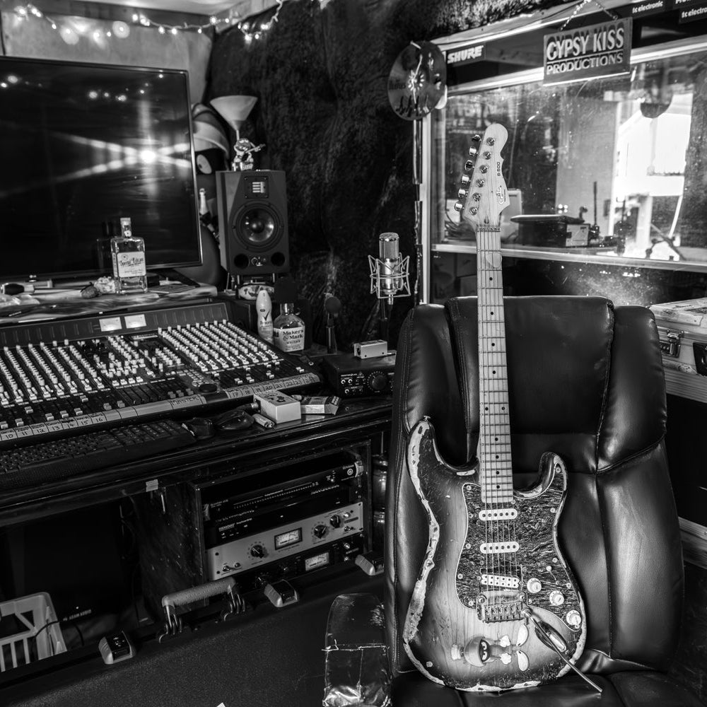 Guitar in a recording studio with mixing console and equipment.